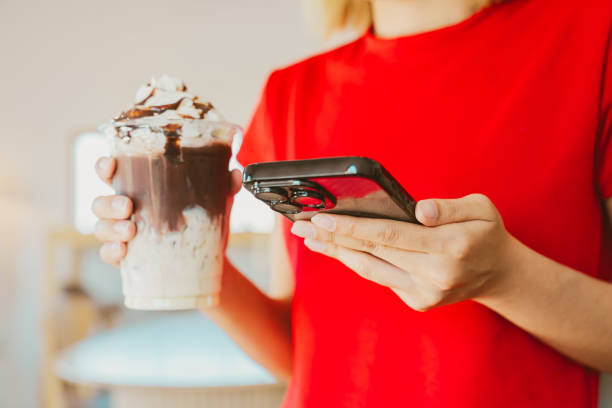 Enjoying delicious chocolate milkshake while using smartphone, this captures moment of indulgence and connection. vibrant red shirt adds pop of color to scene