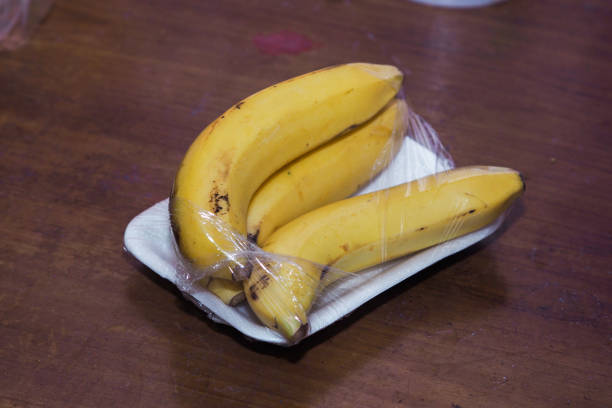 yellow bananas wrapped in plastic on wooden table