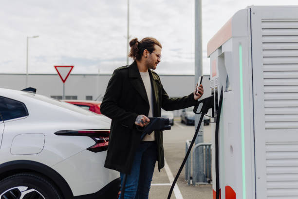 istock Man holding smartphone while charging car at electric vehicle charging station 2188533384