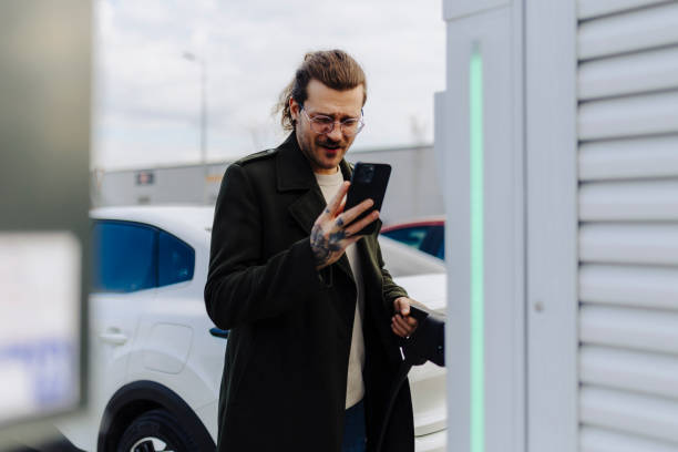 istock Man holding smartphone while charging car at electric vehicle charging station 2188534412