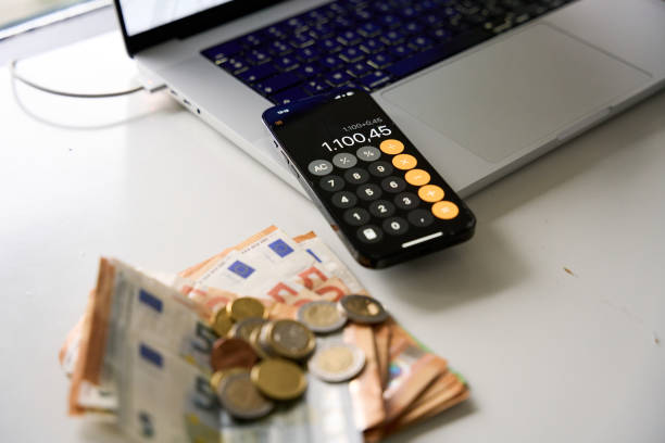 Euro banknotes and coins on an accountant's desk with a laptop and a smartphone displaying a calculator app