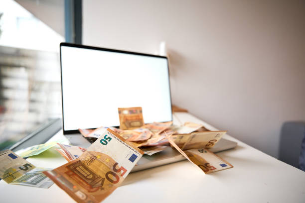 Euro banknotes are scattered on and around a laptop with a blank screen, suggesting online earnings or investments
