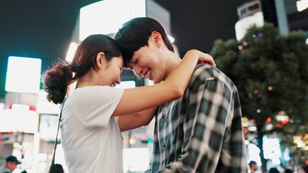 Love, happy couple and hug in city at night for support, loyalty and commitment on vacation. Japanese man, woman and embrace outdoor for romantic relationship, connection and forehead touch on date