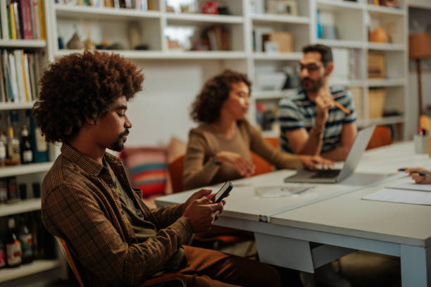 Young man using mobile phone during meeting in modern office