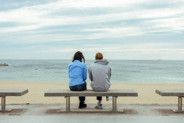 istock Two young adults sitting on a bench and watching the sea 2188551378