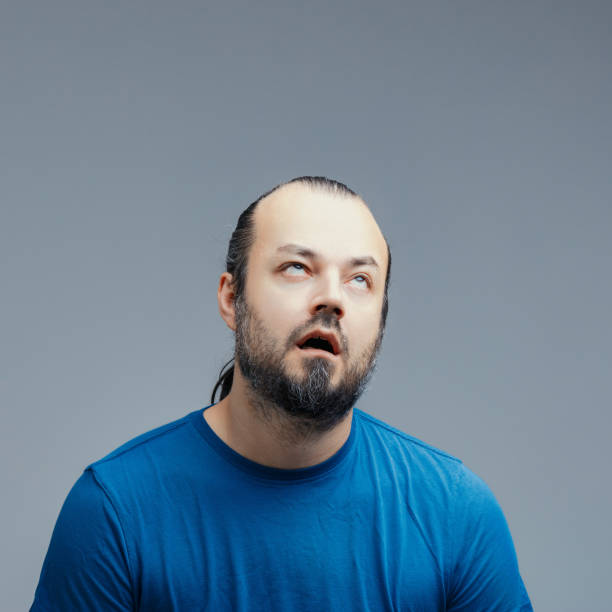 Frustrated man rolling his eyes on a grey background Frustrated young man rolling his eyes and glancing upwards, showcasing boredom and annoyance against a muted grey background, capturing a moment of emotional exhaustion and dissatisfaction rolling eyes irritation displeased facial expression stock pictures, royalty-free photos & images