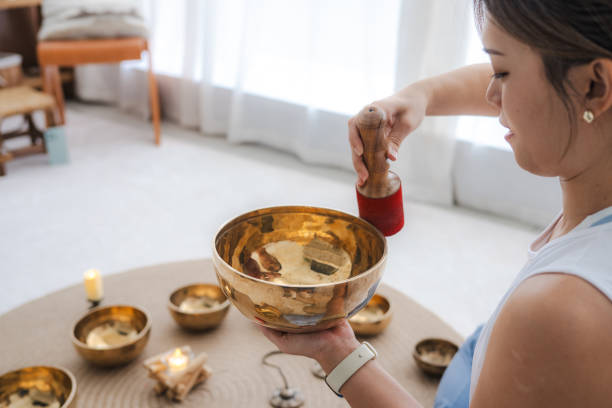 Portrait of beautiful Asian woman playing Tibetan singing bowls for meditation at living room. Tibetan singing bowls can be powerful tools for deepening your meditation practice and cultivating inner peace.