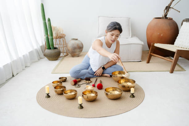 Portrait of beautiful Asian woman playing Tibetan singing bowls for meditation at living room. Tibetan singing bowls can be powerful tools for deepening your meditation practice and cultivating inner peace.