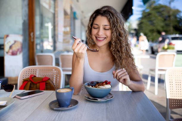 Beautiful woman having breakfast at a cafe and smiling Beautiful woman having breakfast at a cafe and smiling while eating a parfait and drinking coffee - food and drink concepts eating chia seeds stock pictures, royalty-free photos & images