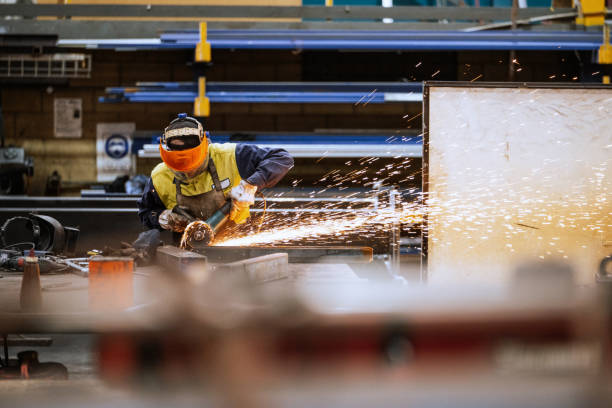 Mature industrial worker in a workshop wearing safety gear using a grinder emitting sparks