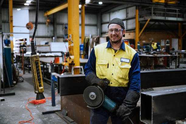 istock Industrial worker in a workshop wearing safety gear holding a grinder and looking at camera 2188581184