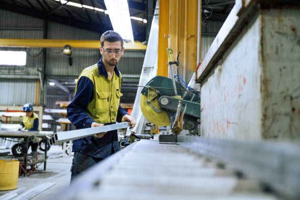 istock Worker in a factory setting adjusting a machine for processing metal materials in an industrial environment with safety gear. Blue collar worker cutting alloy or metal bars 2188581284