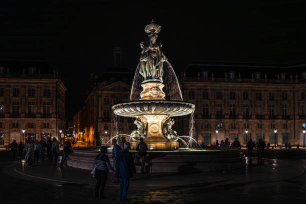 Bordeaux, France. June 5th, 2024: A beautifully illuminated fountain at Place de la Bourse during the night. The intricate statues and cascading water are highlighted against the backdrop of the elegant 18th-century architecture of Bordeaux's iconic square. Visitors gather around the fountain, enjoying the serene ambiance of this historical landmark under city lights.