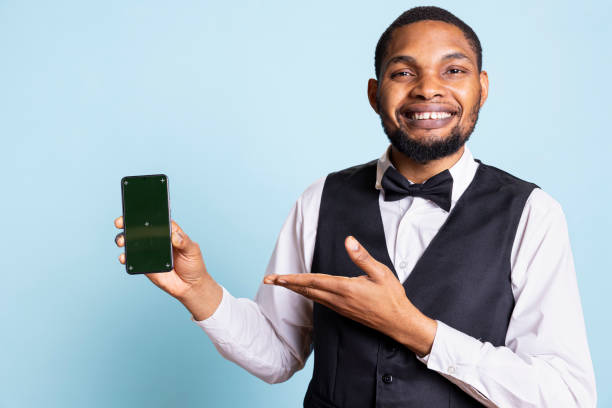 istock Hotel worker bellhop points at phone with isolated mockup display 2188591980