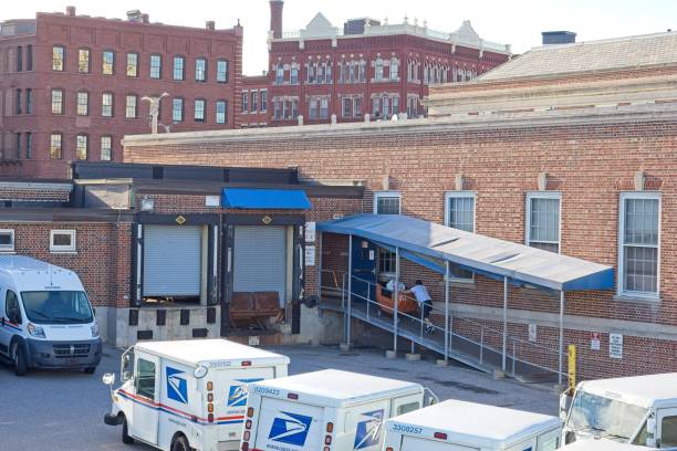 Haverhill, Massachusetts - USA, September 28, 2022. Haverhill United States Post Office loading area. USPS trucks and Postal employee pushing mail packages up ramp into building.