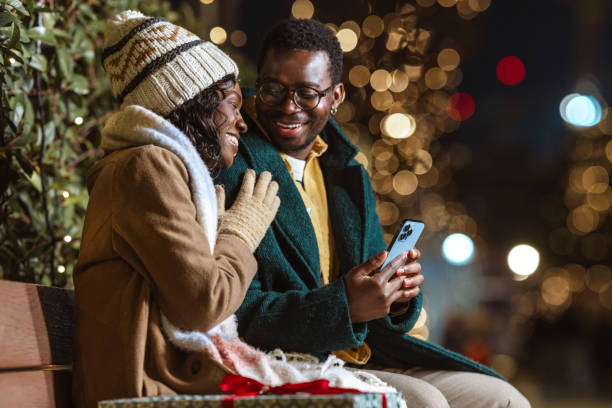 istock Happy couple enjoying Christmas festive lights outdoors and using a smartphone 2188601568