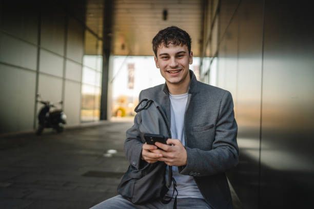 istock Portrait of young man sit on bench with backpack and use mobile phone 2188604767