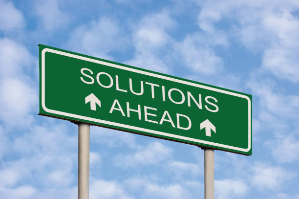 istock Solutions ahead concept green destination signboard road sign, white text frame and arrows, grey pole posts, large detailed horizontal signpost perspective closeup, sunny summer sky cloudscape and clouds background, motivational roadside signage 2188605481