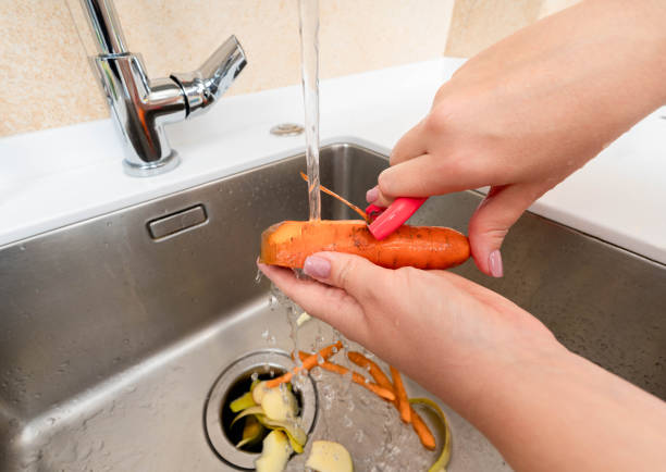 Peeling a fresh carrot under running water with waste collected in a garbage disposer