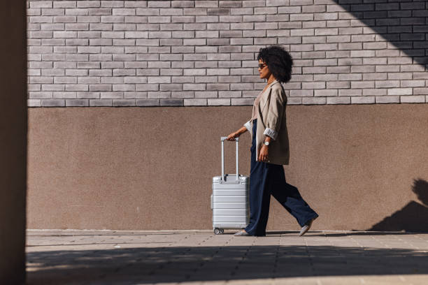 istock Confident Woman Walking With Suitcase Against Brick Wall Background 2188609915