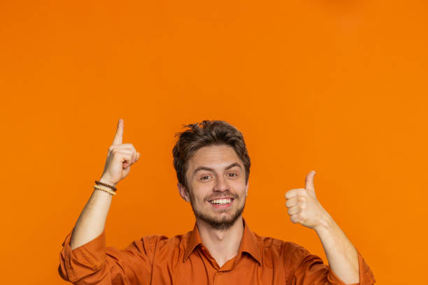 istock Young man showing thumbs up and pointing overhead on blank space place for your advertisement logo 2188615084