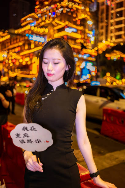 A young woman in black clothing smiles on a city street. The background features a large commercial building with eye-catching billboards. The overall atmosphere is filled with the vitality and fashion of a modern metropolis
