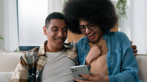 istock African American happy couple having fun using smartphone excited browsing mobile phone app at home girl and guy man and woman talking shopping together buying online ordering delivery family budget 2188616742