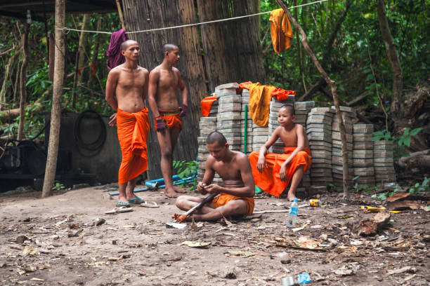 Four monks in orange robes engage in daily activities near Angkor Wat in Cambodia. The serene environment captures the essence of monastic life in this historic site surrounded by nature.