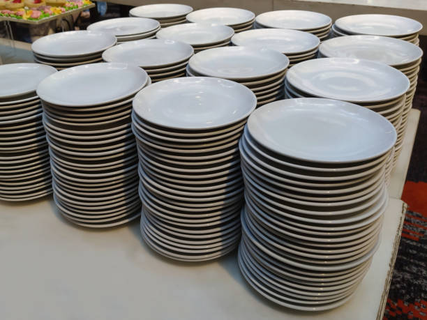 istock stacks of white ceramic plates arranged neatly on a table. Each stack contains a large number of plates, indicating that this setup is likely for a large event or buffet. 2188632952