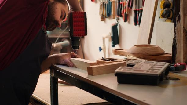 istock Cabinetmaker drills hole into lumber block, doing furniture assembling 2188633770