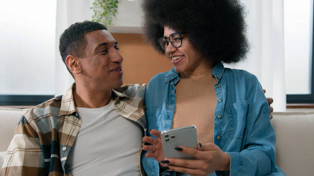 istock African American happy couple having fun using smartphone excited browsing mobile phone app at home girl and guy man and woman talking shopping together buying online ordering delivery family budget 2188637088