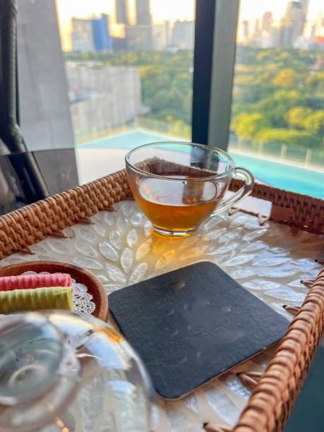 Clear glass cup with tea on a wicker tray by a window with cityscape view