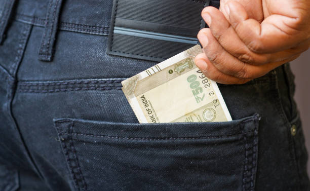 istock Black Indian man putting few Indian rupees notes into his back pocket. Removing money from pocket, hold money. 2188639865