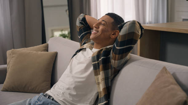 Smiling happy inspired dreaming African American man biracial guy ethnic male relax at home sofa comfortable couch leaning back hands behind head rest apartment weekend resting dream nap closed eyes. High quality 4k footage sonriendo, feliz, inspirado, soñando, hombre afroamericano, hombre birracial, masculino étnico, relájese en casa, sofá, cómodo, sofá, recostado, manos, detrás de la cabeza, descansa, apartamento, fin de semana, descansando, siesta de ensueño, ojos