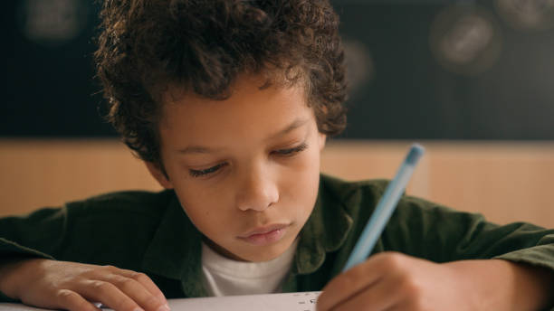 istock Little African American guy boy writing notes task class lesson primary school write in copybook kid schoolboy son child pupil student learning listen teacher studying education sitting at table desk 2188641867