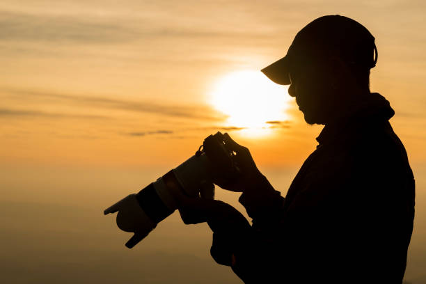 A silhouette of a photographer with a camera against a glowing sunset backdrop. Photographer take photo , silhouette of photographer taking photo in the mountain and sunset .