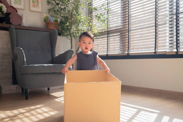 istock Curious wonder asian baby boy unpack home decorating items from moving cardboard box fun and playful kid playing in living rom at home sunset 2188657077