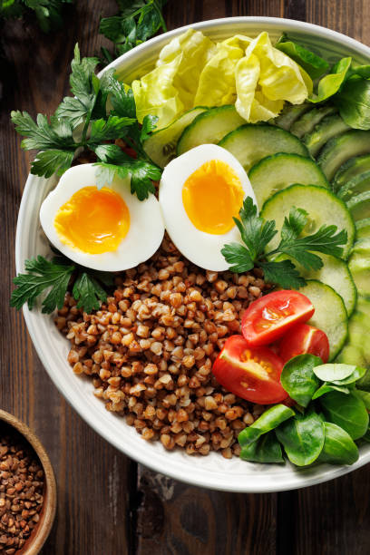 Close up view buckwheat groats with avocado, various vegetables and soft-boiled egg in a ceramic bowl.