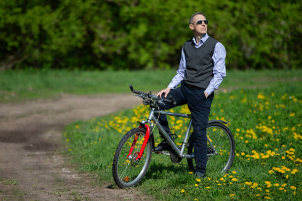 An attractive elderly man in a suit riding a bicycle in a spring meadow.
