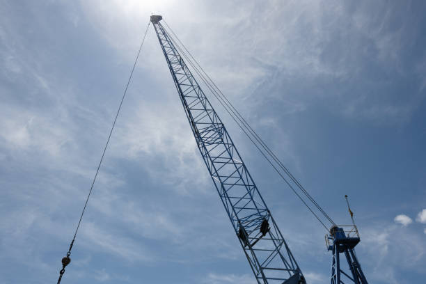 Part of a tall metal construction crane with the sun behind shining through clouds.