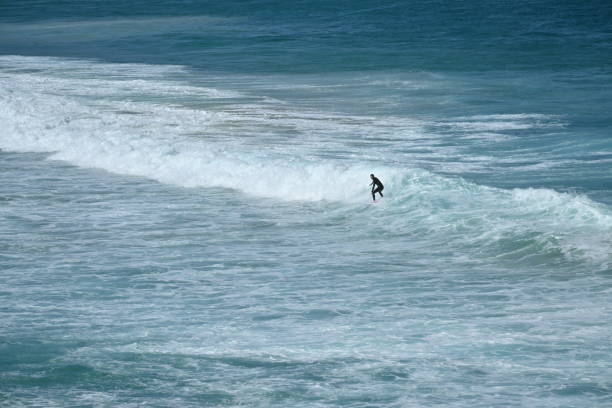 A breaking wave with the small silhouettes of two surfers surfing it