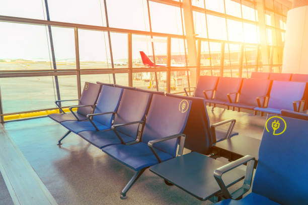 istock Airport waiting area with empty chairs facing large windows. Places with sockets view tarmac departing airplane. Bright sunlight creates outside terminal 2188676621