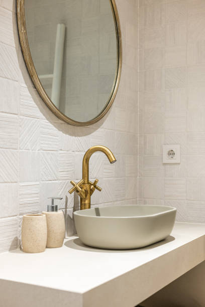 istock Oval stylish sink on white smooth marble countertop in modern bathroom. Copper-colored two-valve faucet blends harmoniously with round mirror hanging on wall and other objects in room. 2188678940