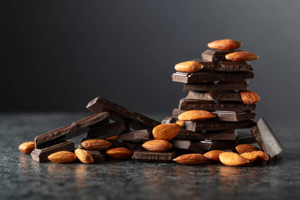 Broken dark chocolate bar with almond on a black background.