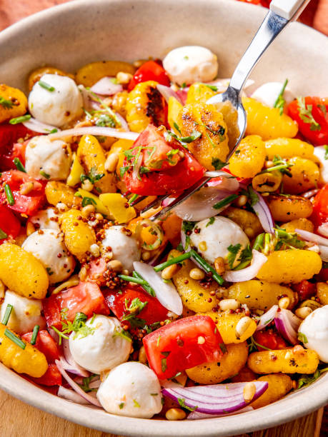 Viral Crispy gnocchi fresh salad served in a bowl with mini mozzarella balls, red onion, cherry tomatoes, pine nuts, and chives mixed with a fork