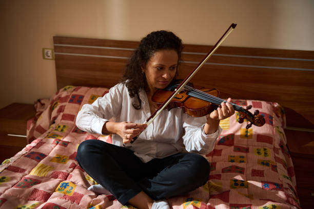istock Woman thoughtfully playing violin while seated on a bed indoors 2188706939