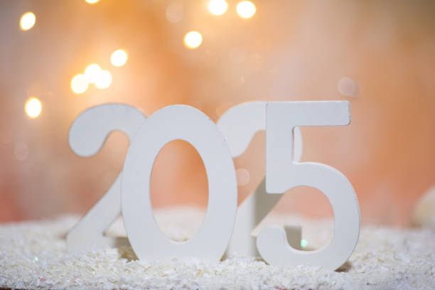 New Year 2025 abstract background: This whimsical image presents large white numbers reading 2015, artistically arranged among synthetic snow and small decorative pine trees with festive bokeh lighting