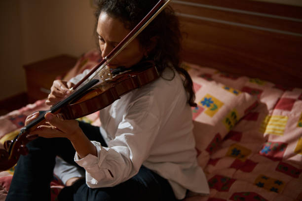 istock Young woman playing violin while sitting on a bed indoors 2188708977