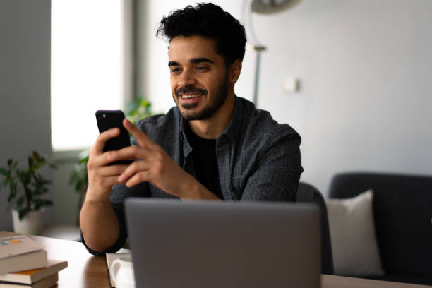 istock University student using smartphone and laptop at home 2188721616