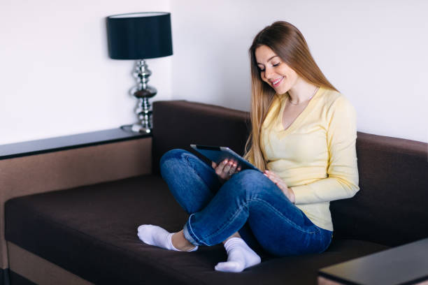 istock Young woman reading e-book on the couch 2188727878